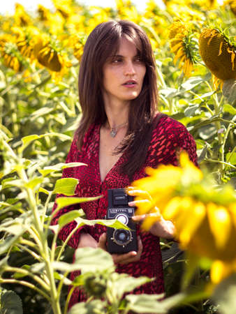 A charming woman in a red dress takes a photo in a field with sunflowers.の写真素材