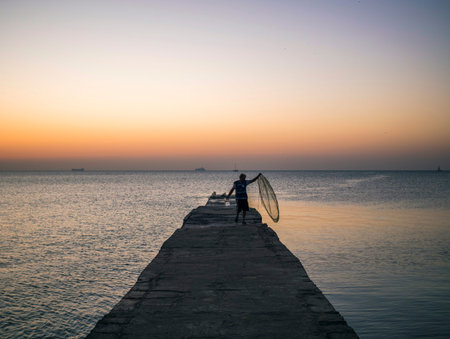 Marine fisherman catches fish from the pier at orange sunset.の写真素材