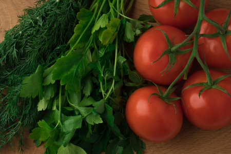 Dill with parsley and five tomatoes on a green branch on a wooden background, set for salad,...