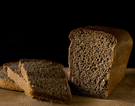 Loaf of black rye bread, cut into pieces, in the shape of a brick on a wooden board, on a black...