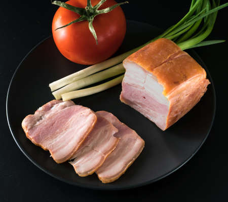 Food, Sliced bacon, tomato green onion, on a black plate on a black backgroundの写真素材