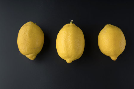 Three whole lemons are arranged in a row, on a black background isolated