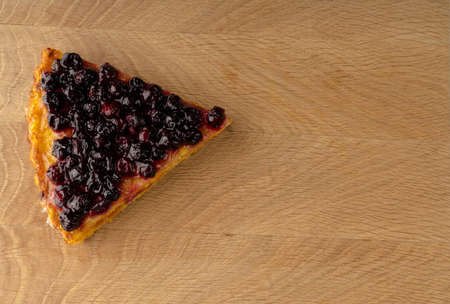 A cut piece of carrot pie, sprinkled with currant berries on top, lies on a wooden board from the side to the leftの写真素材