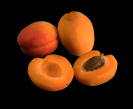 A bunch of ripe Apricot fruits, two whole and one halved, on a black backgroundの写真素材