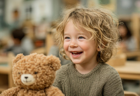 Child with curly hair smiles brightly while holding teddy bear in a vibrant classroom setting, emphasizing joy and the essence of childhood learningの素材