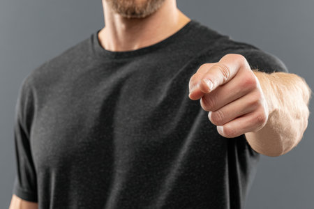 Confident male figure in black t-shirt points at viewer, creating a strong connection, with a smooth gray background enhancing the focus on the gesture and expressionの素材