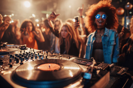 Female DJ enthusiast with curly hair is dancing at a music event, surrounded by an energetic crowd, with turntables and colorful lights creating a festive atmosphereの素材