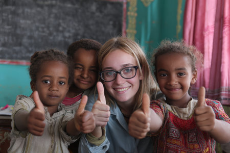 Children and a young woman are smiling and giving thumbs up in a colorful classroom, highlighting friendship and positivity in a learning atmosphereの素材
