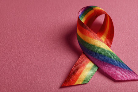 Vibrant rainbow ribbon placed on a pink surface, symbolizing pride and diversity, showcasing support for LGBTQ+ rights and community empowermentの素材