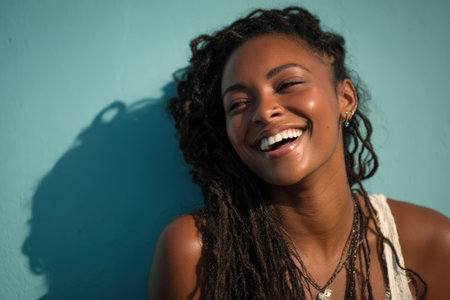 Joyful African American woman with dreadlocks smiles against a turquoise backdrop, showcasing her natural beauty and vibrant personality in a relaxed atmosphereの素材