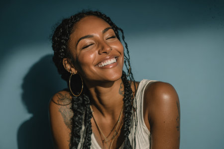 Woman with braided hair smiles brightly, illuminated by soft light against a blue background, conveying happiness and warmth in a peaceful settingの素材