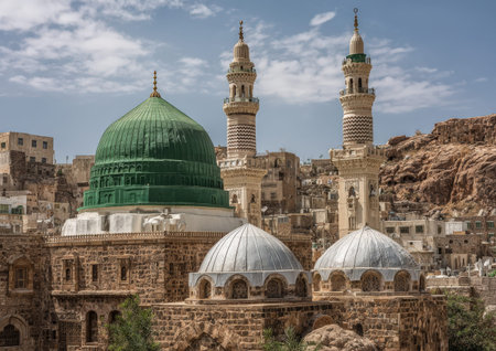 Mosque complex with a striking green dome and twin minarets, nestled among ancient stone structures and rocky landscape, reflecting rich cultural historyの素材