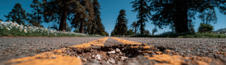 Pothole visible in asphalt on deserted road, framed by trees and clear blue sky, emphasizing the need for road repairs and highlighting environmental impactsの素材
