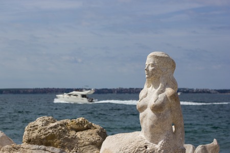 PIRAN, SLOVENIA-Portrait of beautiful mermaid statue on the rocky coastline of Piran, Slovenia. Mermaid sculpture carved out of the stone rocks.の写真素材