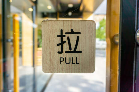 Black Colored Pull Sign in English and Chinese on a Wooden Background on the Glass Doorの写真素材
