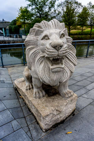 China Stone Lion Sculpture with Open Mouth and River Trees Backgroundの写真素材