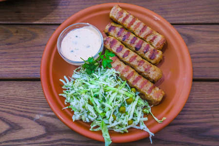 Moldavian Traditional Four Mititei Mici Meat Sticks with Cabbage and a Sauce Dip on a Red Colored Ceramic Plateの写真素材