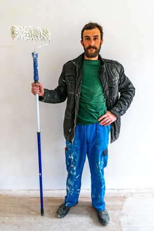 Young Caucasian Brown Haired Man with Beard and Blue Colored Dungarees Working Trousers Standing and...