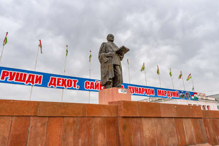 Qurghonteppa Bokhtar Bobojon Ghafurov Statue Surrounded by Tajikistan Flags near City Hall on a Cloudy Rainy Dayのeditorial素材