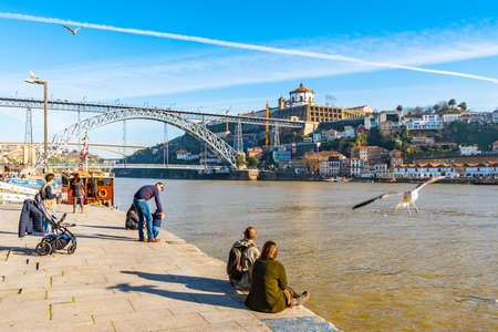 Porto Luis I Bridge Breathtaking Picturesque View with Seagulls and Sitting People at the Shore on a Blue Sky Day in Winterの写真素材