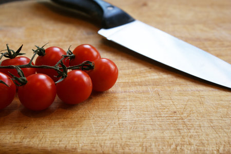 A knife and cherry tomatoes on the vine on a wooden chopping board