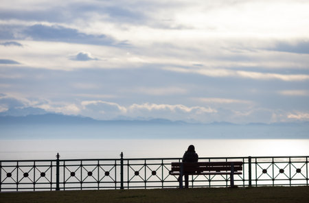 silhouetted woman sitting on bench at lake constance