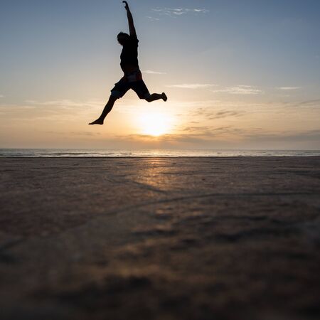 silhouetted man jumping in sunsetの写真素材