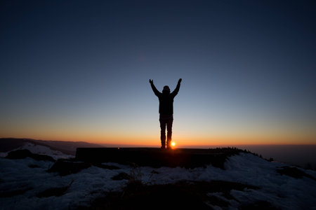 silhouetted man standing in sunset above valleyの写真素材