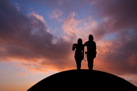 silhouetted couple standing on hill in sunset skyの写真素材