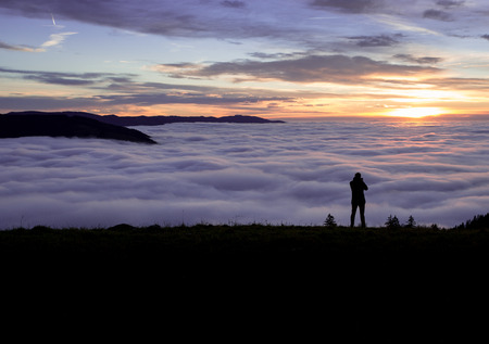 silhouetted photographer standing above fog on hillの写真素材