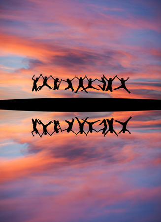 silhouetted teens holding hands and jumping in sunset skyの写真素材