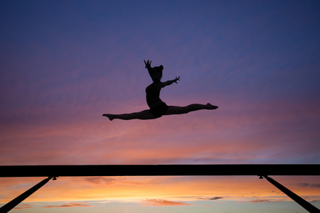 the splits jump on balance beam in sunsetの写真素材