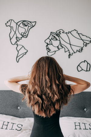 Girl with long and shiny curly hair. The back view of a girl. Woman waking up stretching in bed at...