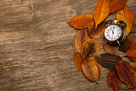 Old clock on a background of yellow leavesの写真素材