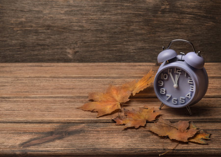 clock on old wooden background decorated with autumn leaves