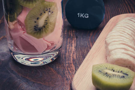 banana, kiwi, smoothie and dumbbell on a wooden background / concept of fitness with dumbbells, smoothie and fruitの写真素材