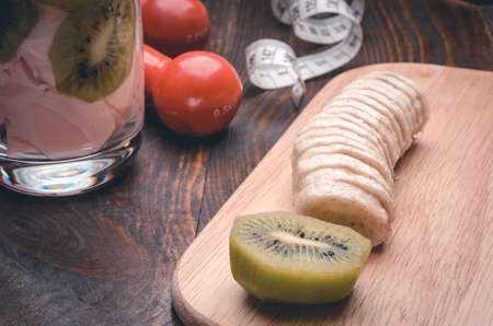kiwi, banana, dumbbell and measurement tape on a wooden surfaceの写真素材