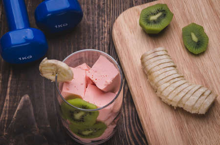 healthy food with smoothies, kiwi, banana and dumbbell on a wooden background / healthy food with smoothies, kiwi, banana and dumbbellの写真素材