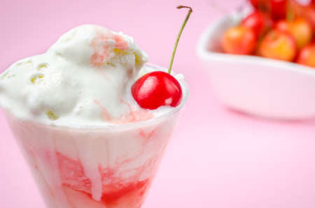 Ice cream in glass and sweet cherry in a white plate / ice cream and a sweet cherry in a white plate on a pink backgroundの写真素材