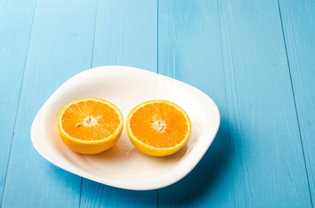 White plate on a blue background with fresh orange / white plate on a blue background with fresh segments of orangeの写真素材