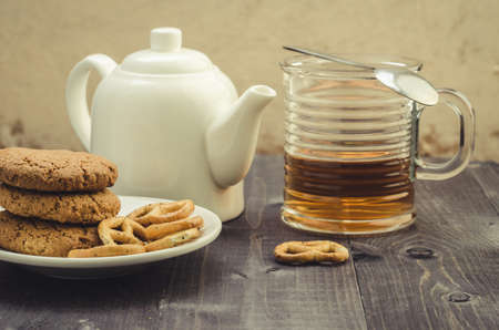 white teapot, cookies and half glass tea/white teapot, cookies and half glass tea on a wooden backgroundの写真素材
