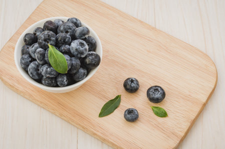 Blueberries with leaves in bowl on a wooden tray white background. Top viewの写真素材