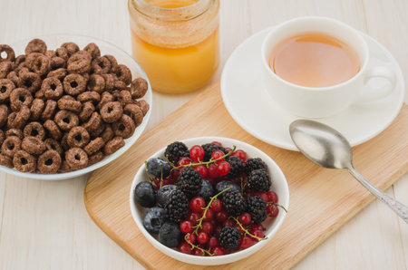 breakfast with flakes, berries, honey and a cup of tea on a wooden tray. selective focus. Top view