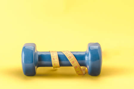 blue dumbbell with yellow centimeter/blue dumbbell with centimeter on a yellow background. Copy spaceの写真素材