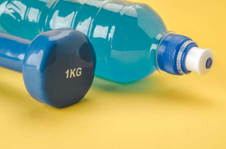 Fitness concept with dumbbell and bottle/blue dumbbell and bottle on a yellow background. selective focusの写真素材