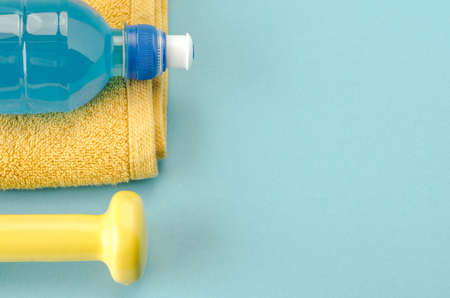 Fitness concept with dumbbell, towel and bottle/yellow dumbbell, towel and bottle on a blue background. Copy space. Top viewの写真素材