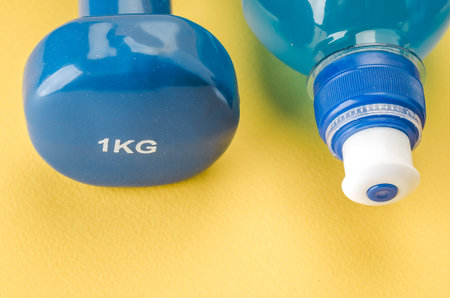 Fitness concept with dumbbell and bottle/blue dumbbell and bottle on a yellow background. Top view の写真素材