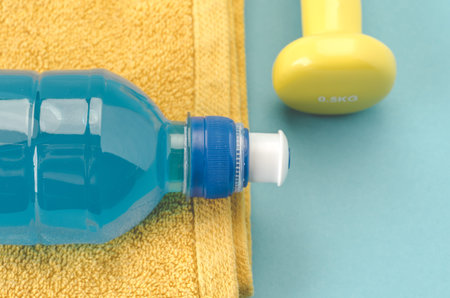 Fitness concept with dumbbell, towel and bottle/yellow dumbbell, towel and bottle on a blue background. Top viewの写真素材