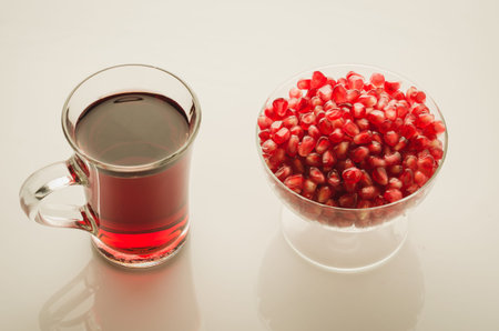 glass of juice and bowl with garnet grains/glass of juice and bowl with garnet grains on a white glossy background. Top viewの写真素材