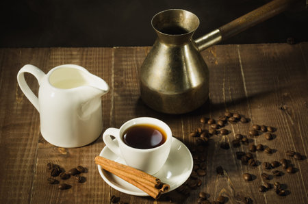 hot coffee cup with cinnamon sticks with a creamer and old pot/hot coffee cup with cinnamon sticks with a creamer and old pot on a dark background. Top viewの写真素材